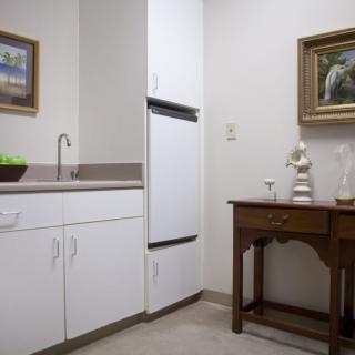 A small kitchenette area with white cabinets, a sink, and decorative artwork on the walls.