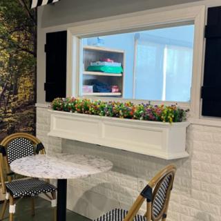 A cozy outdoor cafe seating area with a table and chairs by a window adorned with a flower box.