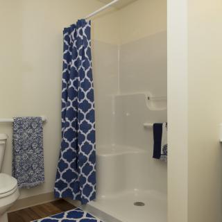 A bathroom featuring a shower with a blue patterned curtain, matching towels, and a bath mat.