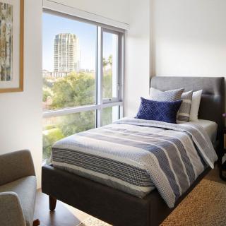A modern bedroom with a single bed and large window offering a city view.