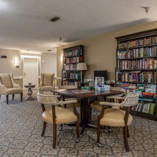 A cozy library room with bookshelves, comfortable chairs, and a central table for reading.