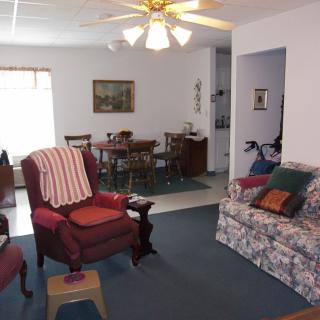 A cozy living room with a floral sofa and armchair, adjacent to a dining area featuring a wooden table and chairs.