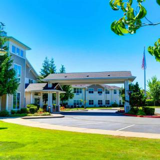 A sunny view of a hotel entrance surrounded by trees and a well-maintained lawn.