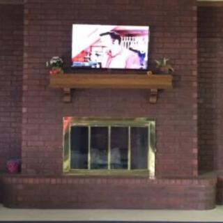 A cozy living room with a brick fireplace featuring a television mounted above the mantel.