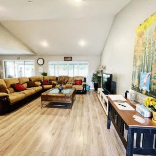 A spacious living room with wooden flooring, featuring a large sofa, coffee table, and a television setup.