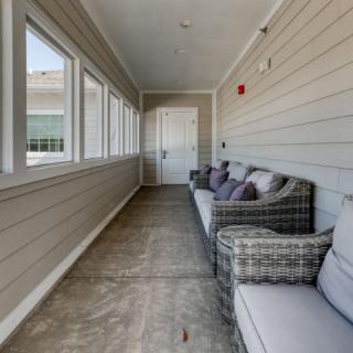 A cozy hallway with wicker sofas and cushions lining one side, facing large windows.