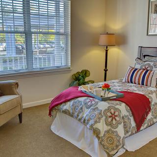 A cozy bedroom with patterned bedding, a floor lamp, and an upholstered chair near the window.