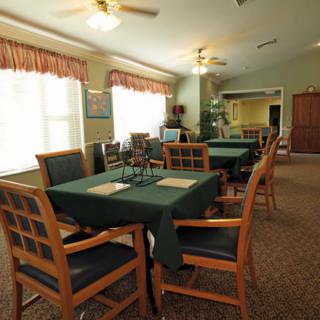 A cozy dining area with neatly arranged tables and chairs, featuring large windows and warm lighting.