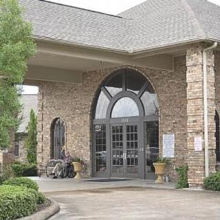 A stone building entrance with large glass doors and neatly arranged landscaping.