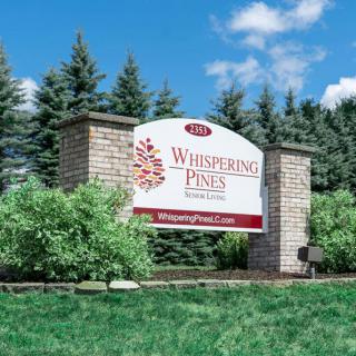 A community entrance sign for Whispering Pines, surrounded by greenery and trees.