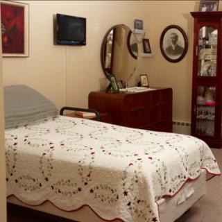 A cozy bedroom with a bed, dresser, and wall-mounted television.