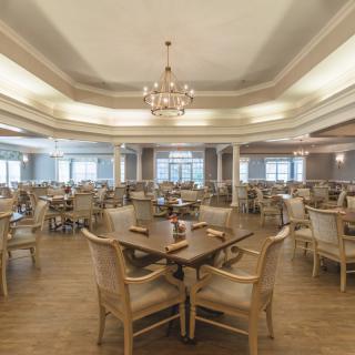 An elegant dining room with neatly arranged tables and chairs, illuminated by a chandelier.