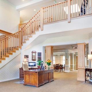 A spacious and well-lit lobby area with a wooden staircase and reception desk.
