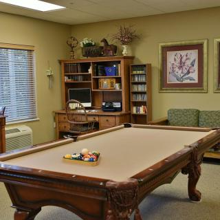 A cozy recreation room with a pool table and a wooden bookshelf featuring a computer, surrounded by artwork on the walls.