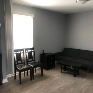 A minimalist living room with gray walls and wooden flooring, featuring a sofa, chairs, and a small table.