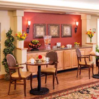 A cozy cafe interior with tables and chairs, decorated with flowers and paintings, featuring a beverage station.
