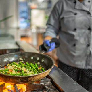 A chef cooking vegetables in a frying pan over a stove in the kitchen.