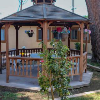 A wooden gazebo in a garden setting, surrounded by greenery.