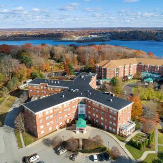 An aerial view of a multi-story building surrounded by autumn trees near a lake.