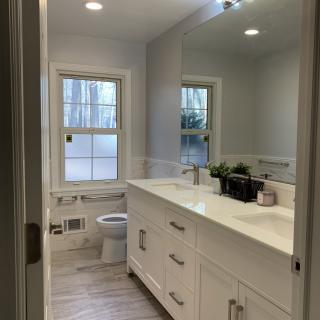 A modern and minimalist bathroom with white cabinetry, a large mirror, and natural light from a window.
