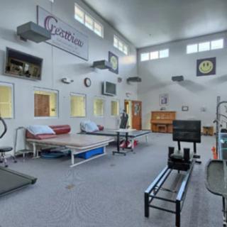 A spacious gym with various exercise equipment, including a treadmill and a rowing machine, illuminated by natural light from large windows.