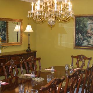 An elegant dining room featuring a chandelier, a long wooden table with chairs, and decorative artwork on the walls.