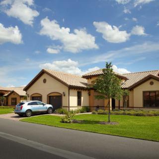 A suburban house with a car parked in the driveway, surrounded by a well-maintained lawn under a cloudy sky.