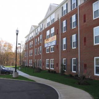 A brick apartment building with a parking lot and sidewalk.
