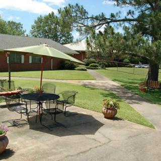 A sunny outdoor patio area with a table, chairs, and an umbrella overlooking a garden and lawn.