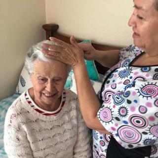A caregiver assisting an elderly woman with grooming, both smiling.