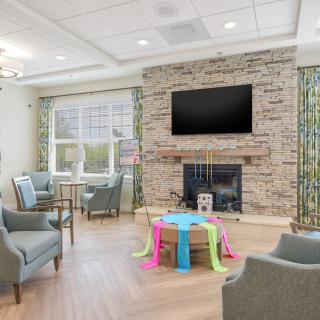 A cozy living room with a stone fireplace, wall-mounted TV, and comfortable seating arranged around a colorful coffee table.
