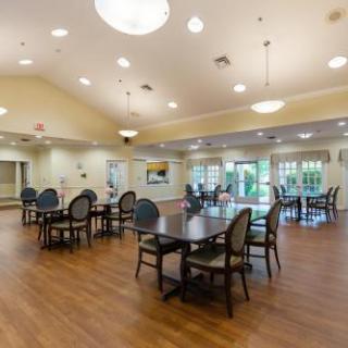 A spacious community lounge featuring dining tables and chairs, bright lighting, and large windows for natural light.