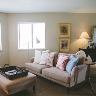 A cozy living room with a sofa, cushions, and a coffee table, warmly lit by a lamp.