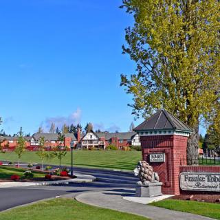 The entrance to a college campus with prominent signage, surrounded by green lawns and trees under a clear blue sky.