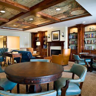 A cozy library interior with wooden furniture, bookshelves, and a fireplace.