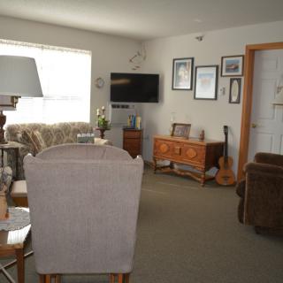 A cozy living room with comfortable seating, featuring a sofa, armchair, and various decor elements such as a television and a guitar.