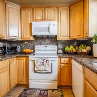 A cozy kitchen with wooden cabinets, a stove, and a microwave, adorned with fresh fruits on the countertop.