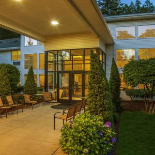 A well-lit hotel entrance with outdoor seating surrounded by manicured landscaping in the evening.