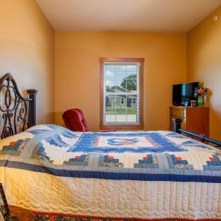 A cozy bedroom with a quilt-covered bed, TV, and window view.