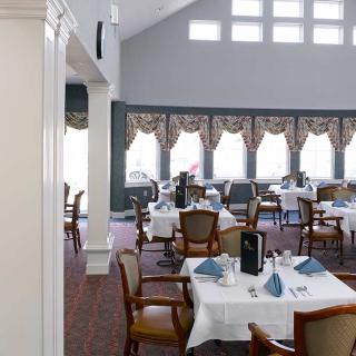 An elegant dining room with neatly arranged tables and chairs, featuring large windows adorned with decorative curtains.