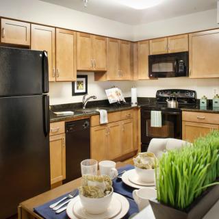 A modern kitchen with wooden cabinets, black appliances, and a neatly set dining table.