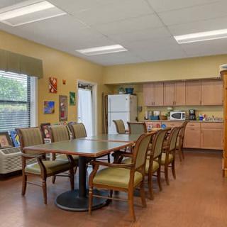 A cozy dining area with a large table and several chairs, featuring a kitchen setup with cabinets and a microwave.