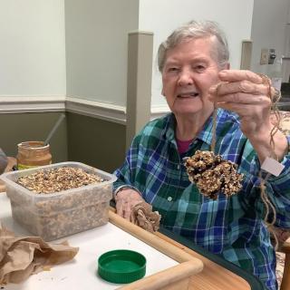 An elderly person smiling while working on a bead craft project indoors.