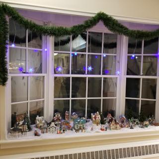 A festive window display featuring garlands, string lights, and charming miniature houses adorned for the holiday season.