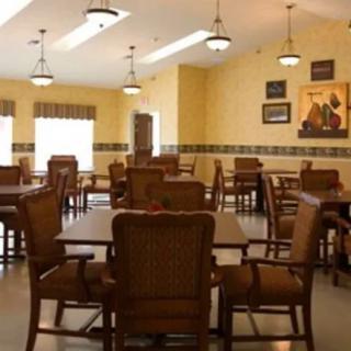 An empty dining room with wooden tables and chairs, warmly lit by ceiling fixtures.