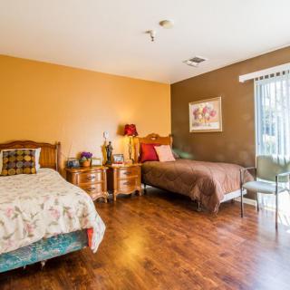 A cozy bedroom with two beds and wooden flooring, decorated with nightstands, lamps, and a window allowing natural light.