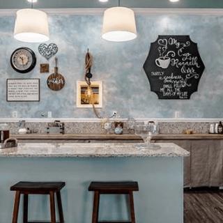 A cozy kitchen setting featuring a marble countertop, decorative wall art, and two stools under stylish pendant lighting.