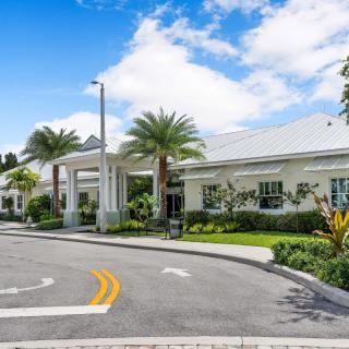 A modern building surrounded by palm trees with a curved road leading up to it under a partly cloudy sky.