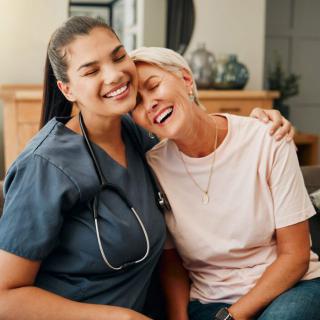 A smiling nurse sitting with a happy woman in a home setting.