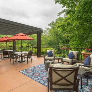 A spacious outdoor patio featuring comfortable furniture and red umbrellas, surrounded by lush greenery.